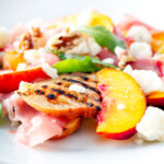 Overhead main course summer salad with pickled peaches, ham and goats cheese.
