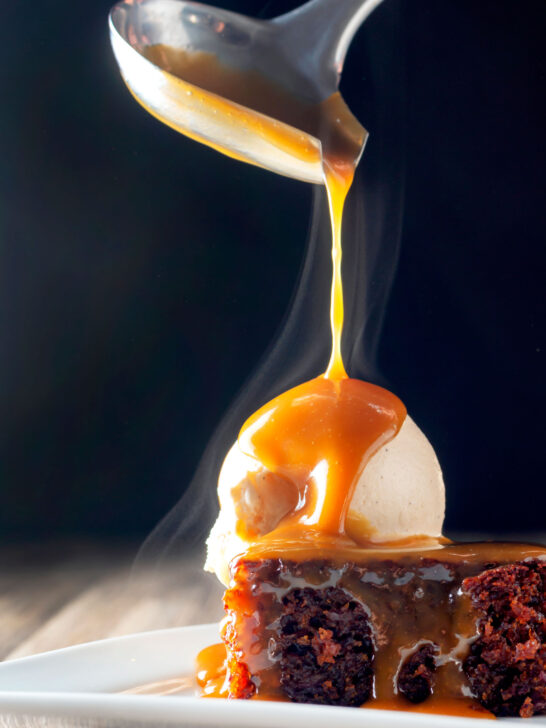 Hot caramel sauce being poured over British sticky toffee pudding and vanilla ice cream.