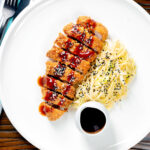 Overhead Japanese Tonkatsu pork cutlet served with katsu sauce and "soused" cabbage featuring a title overlay.