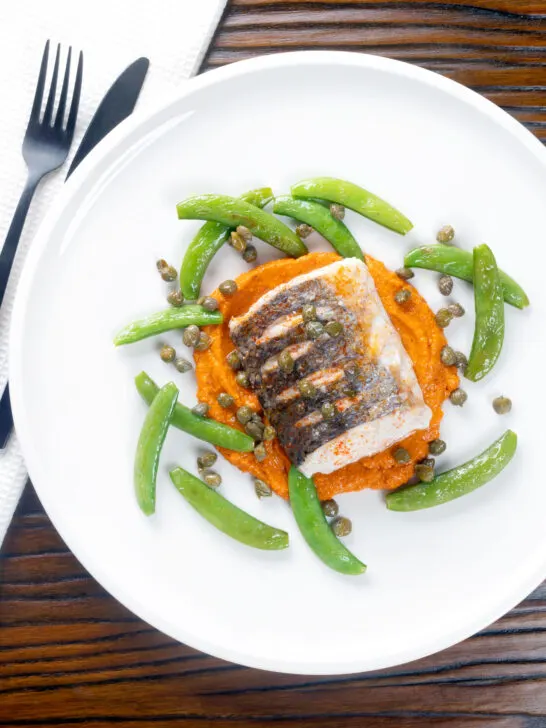 Overhead baked or roasted hake with romesco sauce, capers and sugar snap peas.