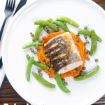 Overhead baked or roasted hake with romesco sauce, capers and sugar snap peas featuring a title overlay.
