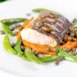 Baked or roasted hake with romesco sauce, capers and sugar snap peas.