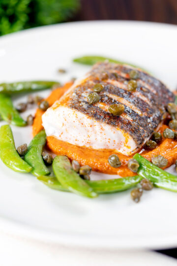 Baked or roasted hake with romesco sauce, capers and sugar snap peas.