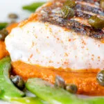 Close-up baked or roasted hake with romesco sauce, capers and sugar snap peas.