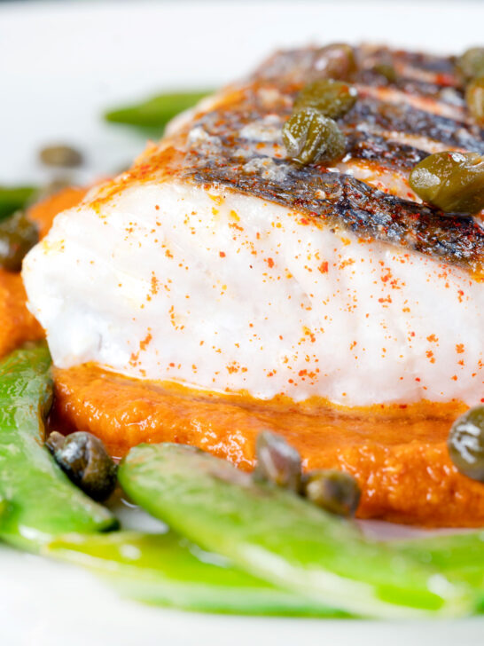 Close-up baked or roasted hake with romesco sauce, capers and sugar snap peas.