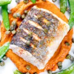Overhead close-up roasted hake with romesco sauce, capers and sugar snap peas.