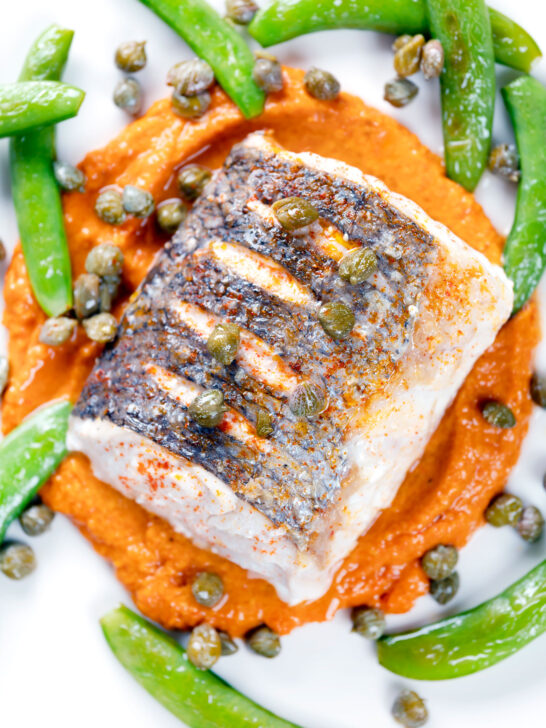 Overhead close-up roasted hake with romesco sauce, capers and sugar snap peas.