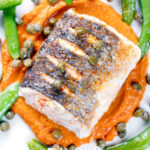 Overhead close-up roasted hake with romesco sauce, capers and sugar snap peas featuring a title overlay.