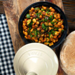 Overhead chickpea tagine with courgettes, harissa and preserved lemons served with flatbreads.