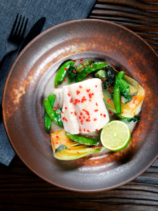 Overhead cod loin poached in coconut milk with pak choi and sugar snap peas.