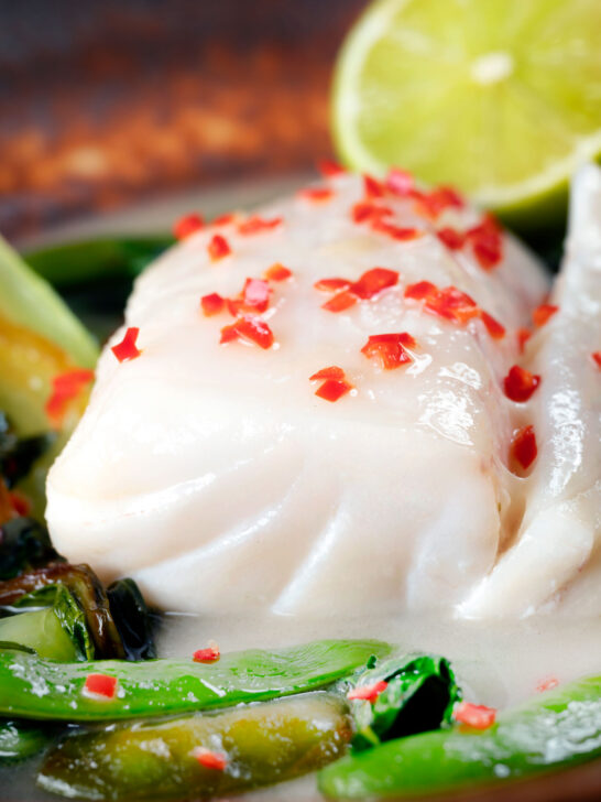 Close-up cod loin poached in coconut milk with fresh chilli.