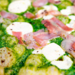 Close up thick crust goat cheese pizza with streaky bacon and rocket pesto.