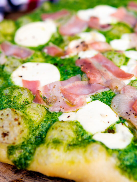 Close up thick crust goat cheese pizza with streaky bacon and rocket pesto.