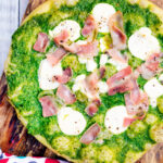 Overhead thick crust goat cheese pizza with streaky bacon and rocket pesto.