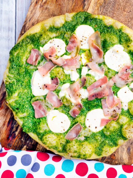 Overhead thick crust goat cheese pizza with streaky bacon and rocket pesto.