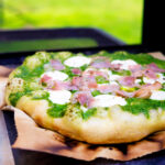 Thick crust goat cheese pizza with streaky bacon and rocket pesto.