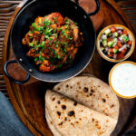 Overhead spicy halloumi curry served with chapatis, mint raita and kachumber salad.