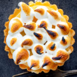 Overhead mini lemon meringue pie tartlet with Italian meringue featuring a title overlay.