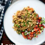 Overhead lamb kabsa, Saudi Arabian rice with almonds and raisins served with chopped salad featuring a title overlay.