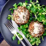 Overhead beef mince stuffed Portobello mushrooms with parmesan cheese and lambs lettuce featuring a title overlay.