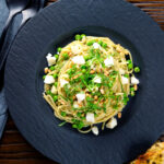 Overhead pesto pasta with aged goat cheese and peas served with garlic bread.