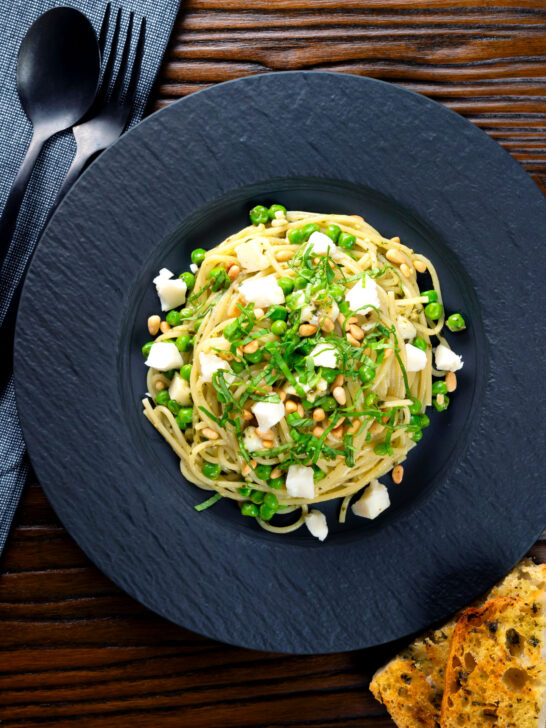 Overhead pesto pasta with aged goat cheese and peas served with garlic bread.