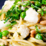 Close-up pesto pasta with aged goat cheese and peas served with garlic bread.