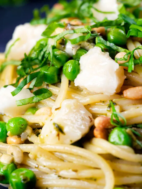 Close-up pesto pasta with aged goat cheese and peas served with garlic bread.
