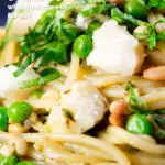 Close-up pesto pasta with aged goat cheese and peas served with garlic bread, featuring a title overlay.