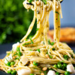 Pesto pasta (spaghetti) with goat cheese and peas on a fork.