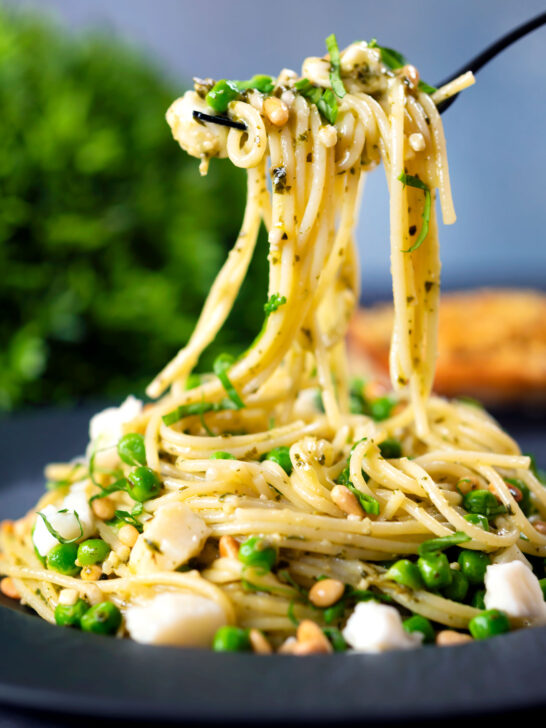 Pesto pasta (spaghetti) with goat cheese and peas on a fork.