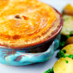 Close-up rabbit pot pie with a suet crust served with buttery potatoes and peas.