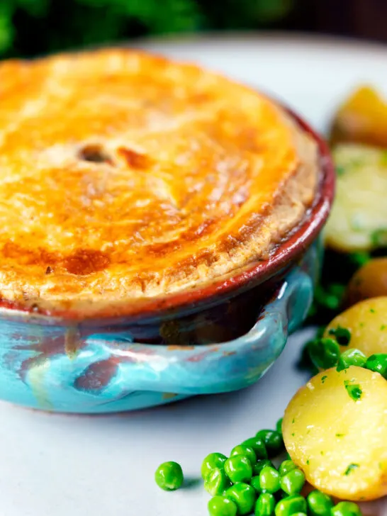 Close-up rabbit pot pie with a suet crust served with buttery potatoes and peas.