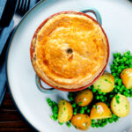 Overhead rabbit pot pie with a suet crust served with buttery potatoes and peas.