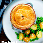 Overhead rabbit pot pie with a suet crust served with buttery potatoes and peas featuring a title overlay.