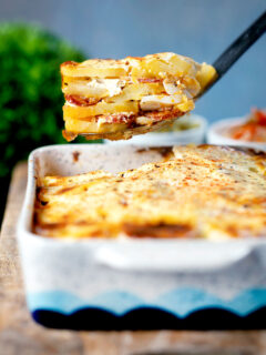 Spoon of potato bake being take out of a bowl of Hungarian rakott krumpli.