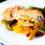 Hungarian layered potato bake, rakott krumpli served on a plate with pickles.