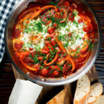 Overhead shakshuka, a baked tomato and egg stew with chorizo sausage featuring a title overlay.