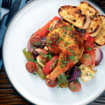 Overhead Spanish chicken and chorizo tray bake with vegetables served with toasted bread.