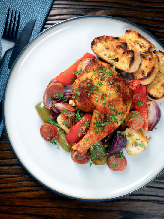 Overhead Spanish chicken and chorizo tray bake with vegetables served with toasted bread.