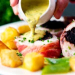 Chive and mustard sauce being poured over bacon wrapped black pudding stuffed chicken breast.