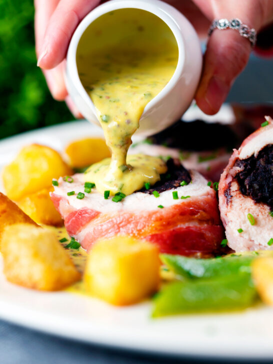 Chive and mustard sauce being poured over bacon wrapped black pudding stuffed chicken breast.