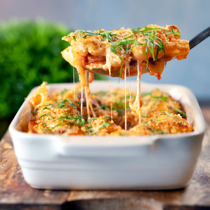 Cheesy chicken and chorizo sausage pasta bake being served with a spoon.