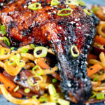 Close-up Chinese style char siu chicken leg served with sweet and sour noodles.