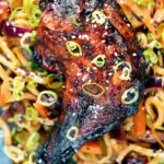 Overhead close-up Chinese style char siu chicken leg served with sweet and sour noodles.