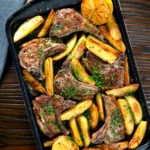Overhead Greek lamb chops with lemon and garlic potatoes on a baking sheet.
