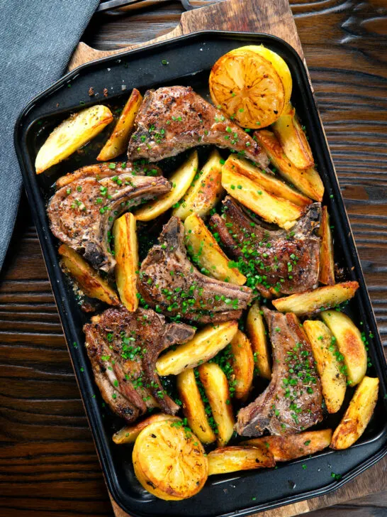 Overhead Greek lamb chops with lemon and garlic potatoes on a baking sheet.