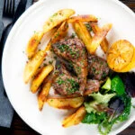 Overhead Greek lamb chops served with roasted garlic potatoes and seared lemon.