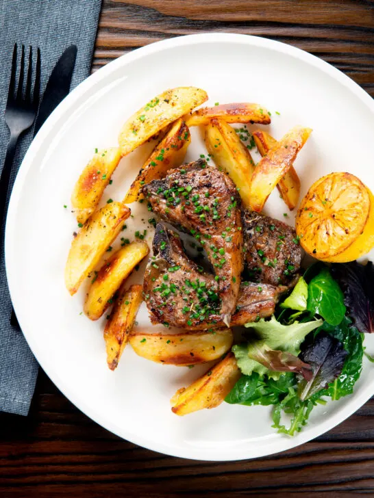 Overhead Greek lamb chops served with roasted garlic potatoes and seared lemon.