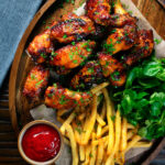Overhead honey and sriracha glazed chicken wings served with French fries.